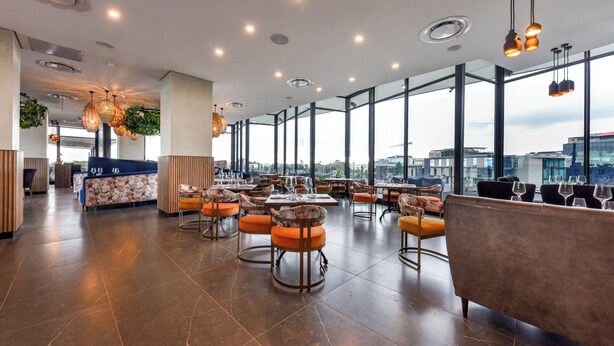 Un restaurante espacioso con techos altos, ventanas amplias e iluminación moderna.