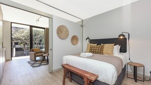 Un dormitorio moderno con una cama grande, una banca, un escritorio y vistas al exterior.