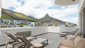 Terraza en la azotea con sillones de descanso y un sofá, con vistas a un paisaje urbano y una montaña.