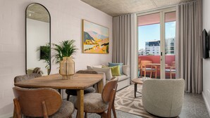 Una sala moderna con una mesa de comedor de madera, asientos cómodos, un espejo grande, un cuadro y vistas de la ciudad a través de amplios ventanales.