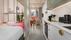 Habitación de hotel moderna con cama, un pequeño comedor, kitchenette y vistas de la ciudad.