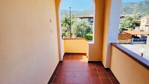 Un couloir au sol carrelé, avec un plafond blanc et une vue sur un quartier résidentiel, visible à travers une arche.