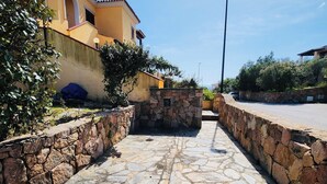 Un chemin pavé mène à un bâtiment dont un côté est bordé d’un mur de pierre et l’autre, d’une rue.