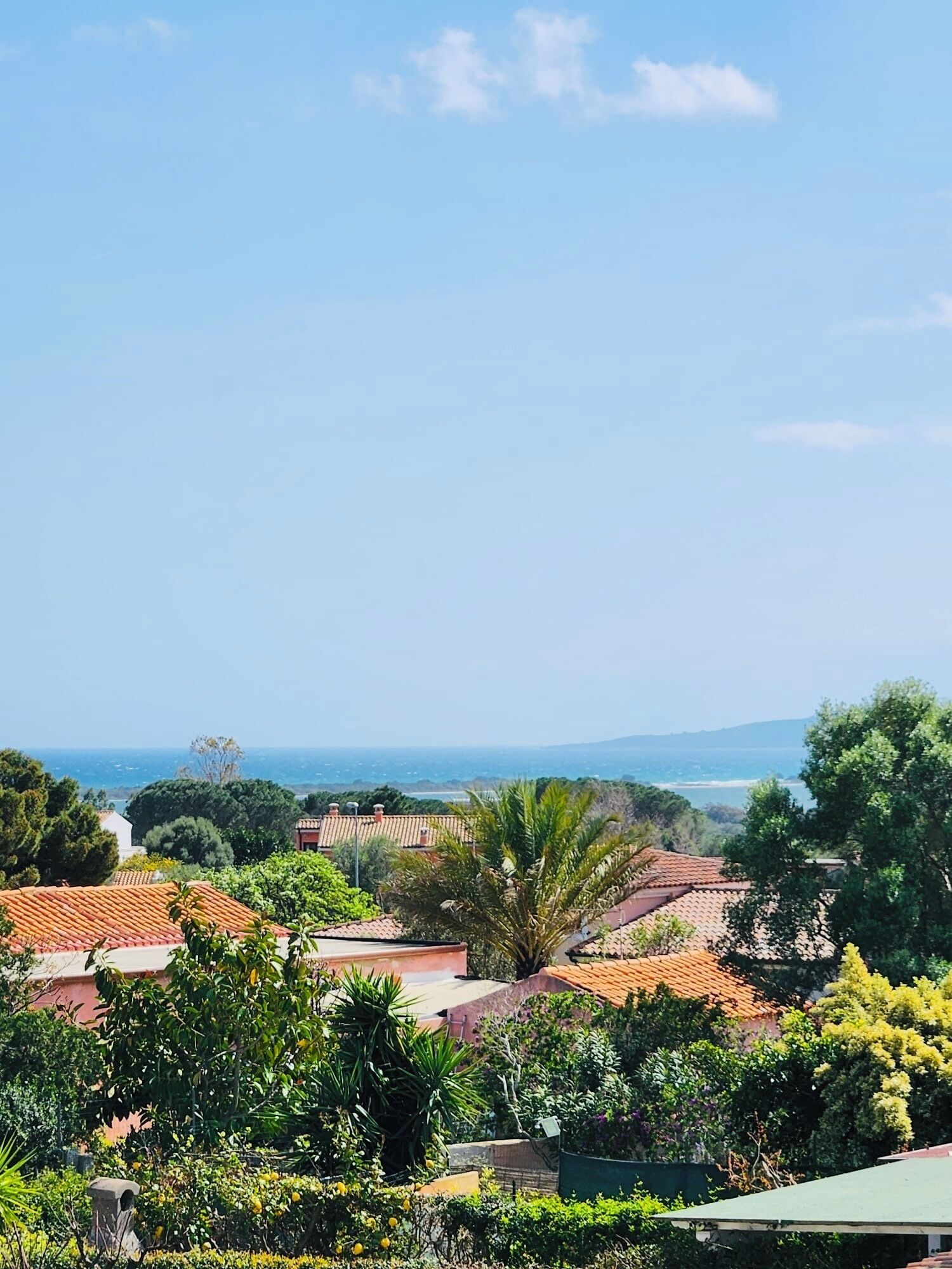 Ein Küstenwohngebiet mit Häusern mit Terrakotta-Dächern, üppigem Grün und freiem Blick auf das Meer.