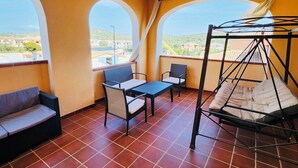 Un balcon avec un canapé, des chaises, une table et un fauteuil suspendu.