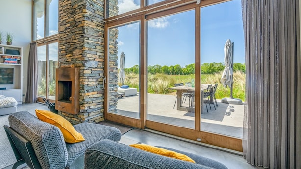 A modern living room with a stone fireplace, large sliding glass doors, and a view of the outdoors. - Luxurious and Sustainable 6-person Holiday Villa (De Koog)