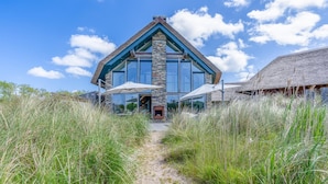 A modern house with a stone facade, large windows, and a thatched roof structure. - Luxurious and Sustainable 6-person Holiday Villa (De Koog)