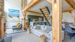 A spacious living area with a white sofa, wooden accents, a staircase, and a kitchen in the background. - Luxurious and Sustainable 6-person Holiday Villa (De Koog)
