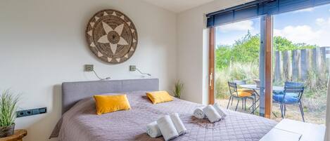 A bedroom with a large bed, two pillows, a wall art piece, and a view of the outside.