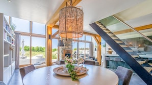 A modern dining area with a round table, wicker chandelier, and large windows offering a view of the outdoors. - Luxurious and Sustainable 6-person Holiday Villa (De Koog)