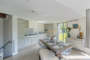 A modern kitchen with white cabinetry, a dining area with a wooden table set for six, and a large window providing natural light.