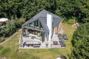 Ein modernes Haus mit einer großen Terrasse, einer wintergartenartigen Veranda und einem Schornstein.