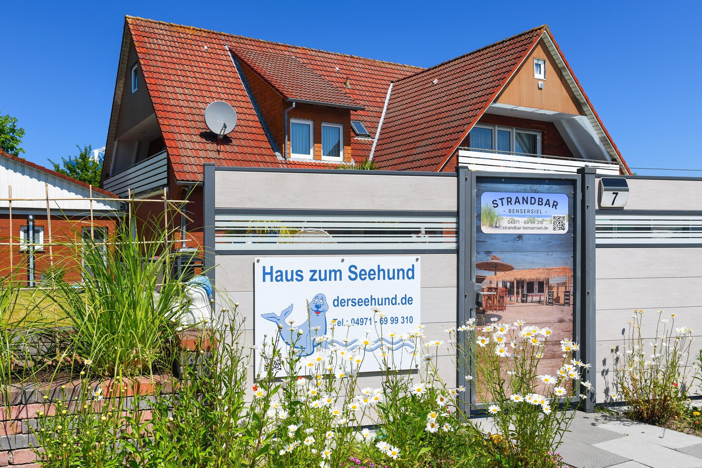 A building with a red-tiled roof, a sign for 'Haus zum Seehund,' and a 'Strandbar' sign.