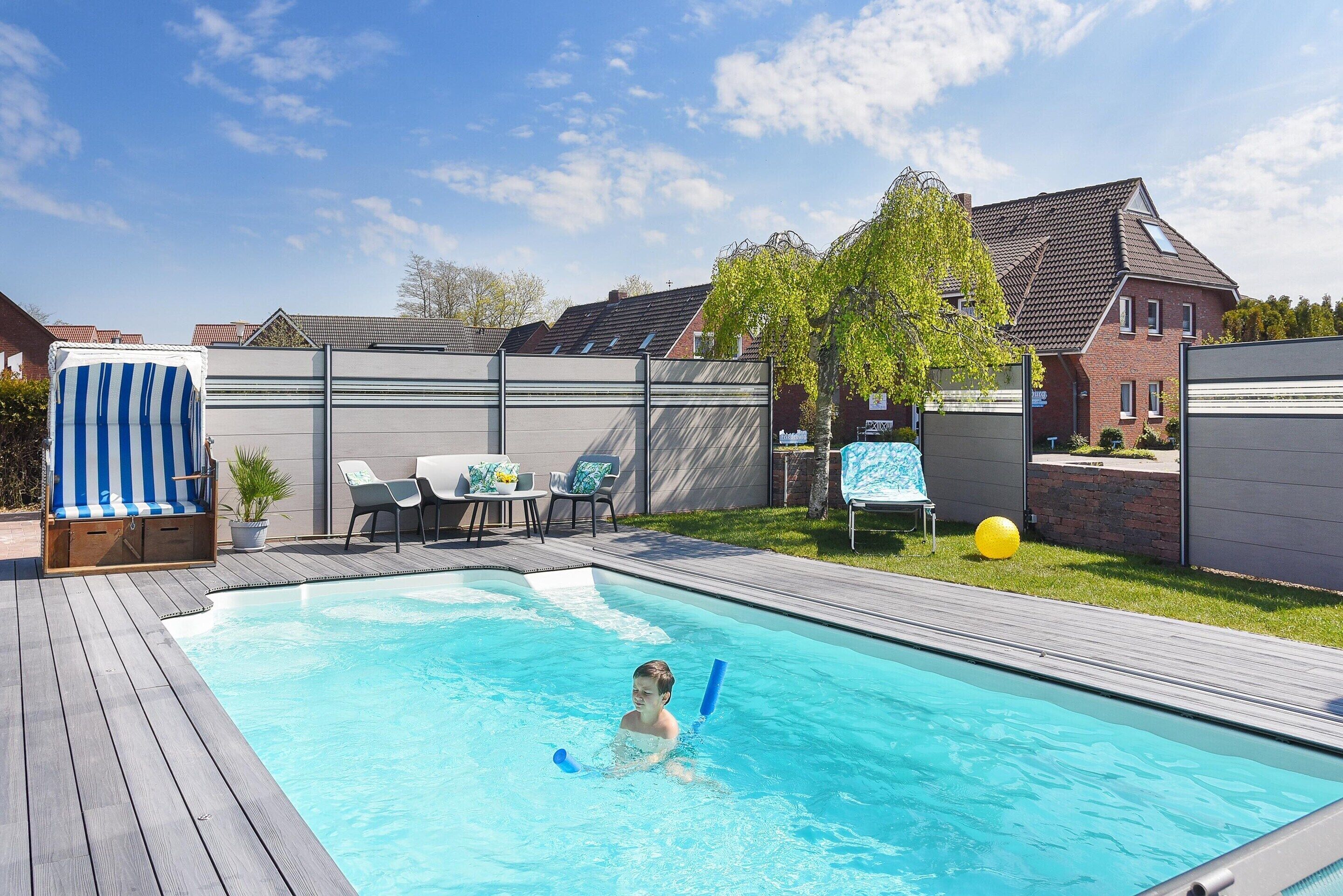 A swimming pool with a wooden deck, lounge chairs, and a covered seating area.