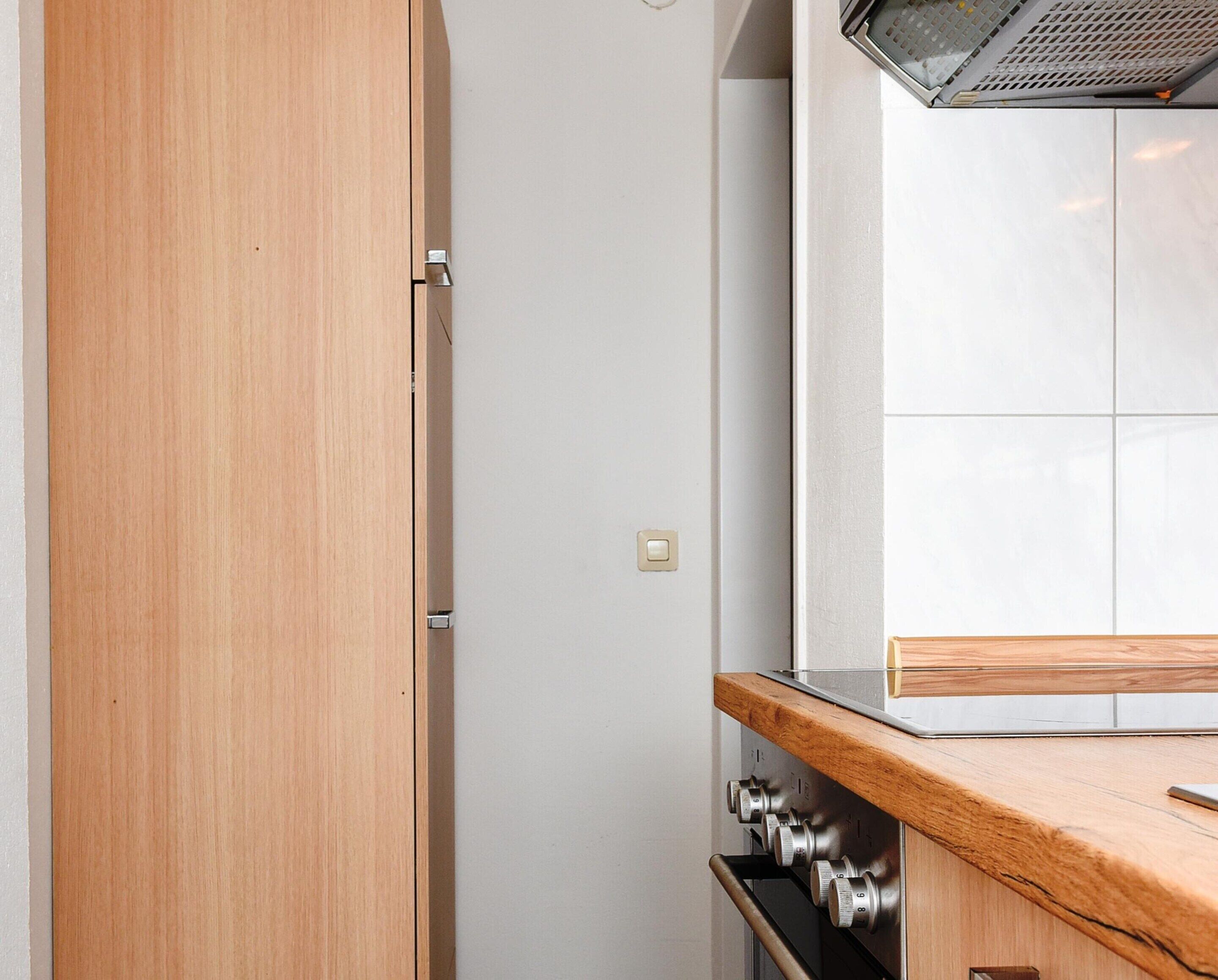 A kitchen with a wooden cabinet door, a stainless steel oven, and a tiled backsplash.