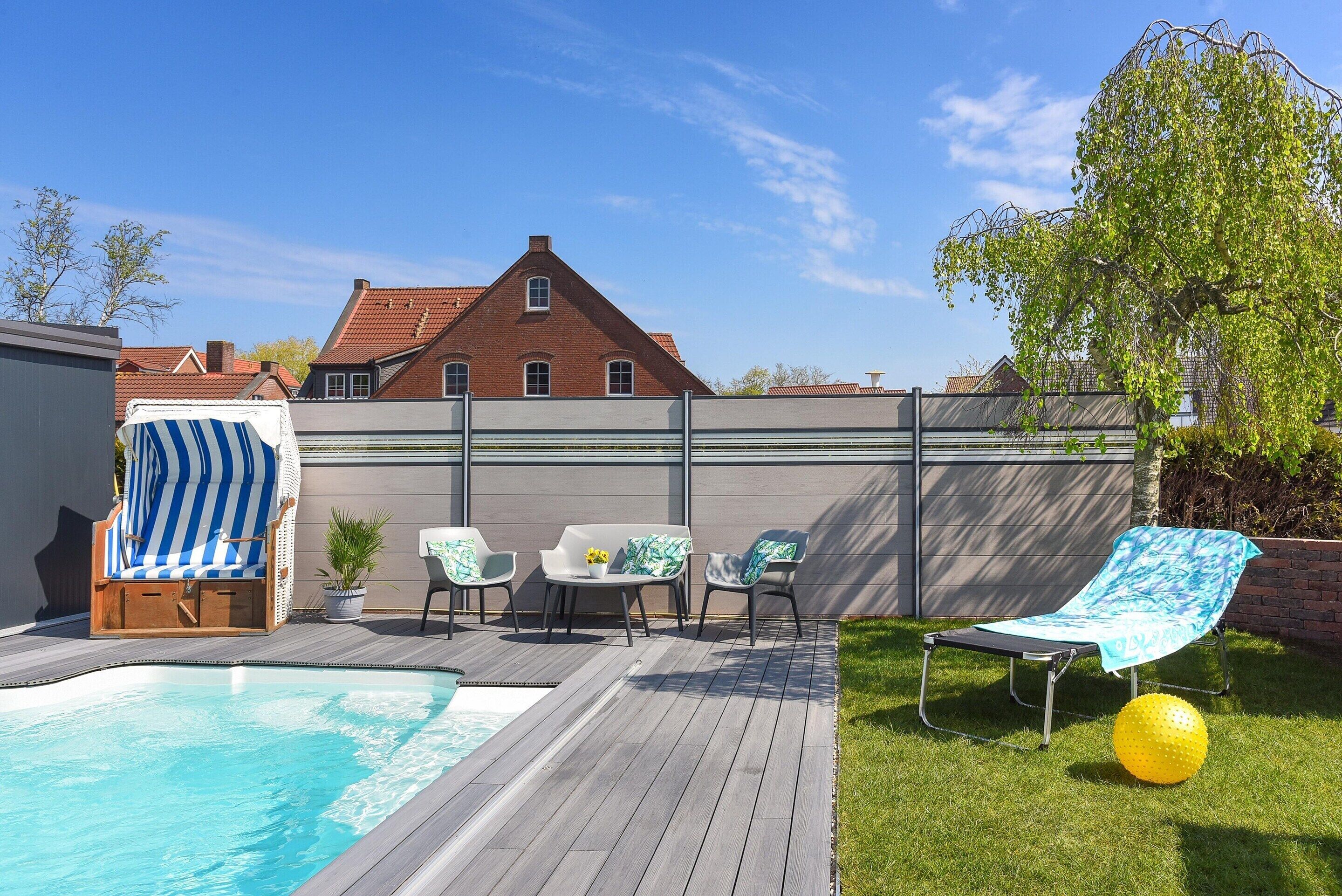 A backyard with a swimming pool, wooden deck, lounge chairs, and a covered seating area.