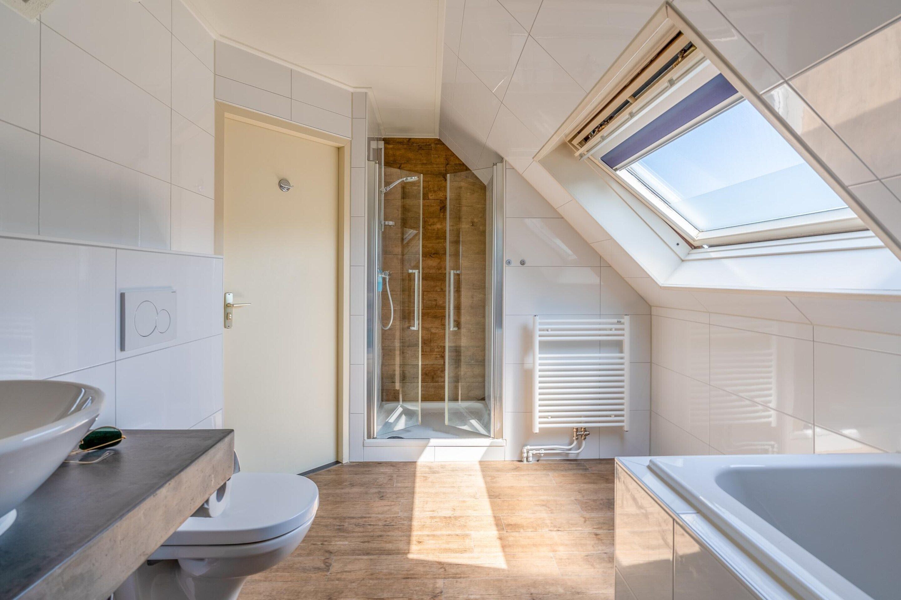 A modern bathroom with a skylight, a shower, a toilet, and a bathtub.