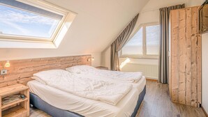 Een slaapkamer met twee bedden, een dakraam, een houten hoofdbord, bedlampjes en een houten garderobe.