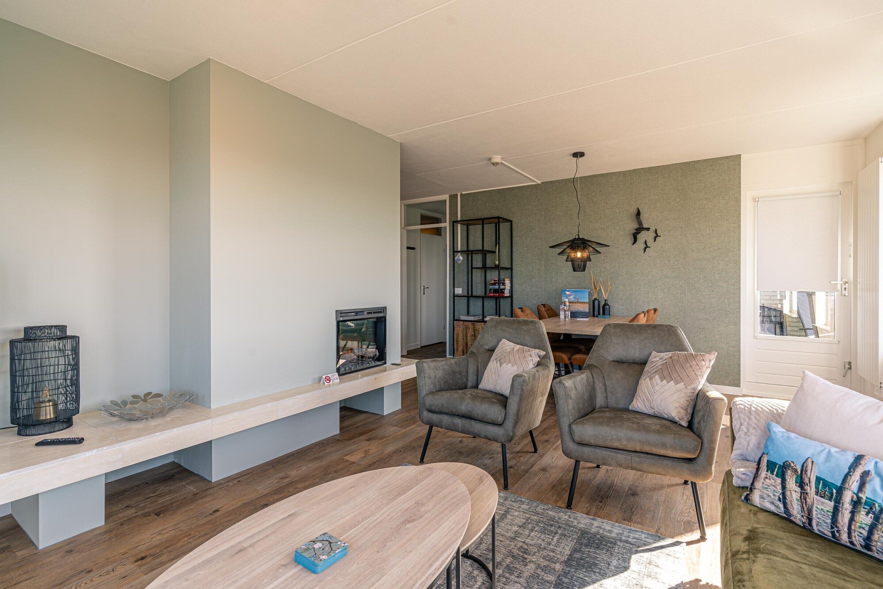 A modern living room with a fireplace, two armchairs, a sofa, and a dining area.