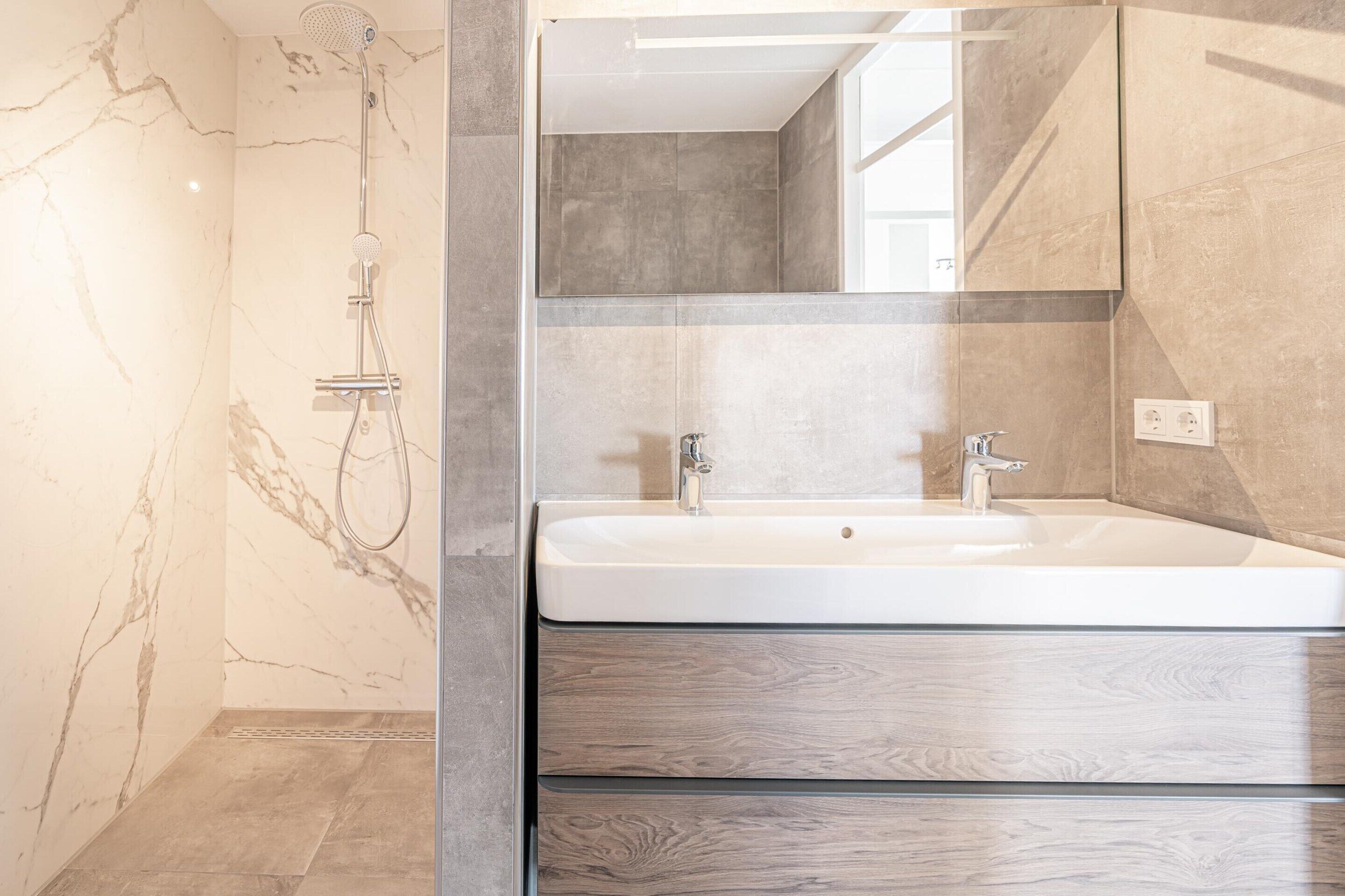 A modern bathroom with a marble shower, a large sink, and a mirror.