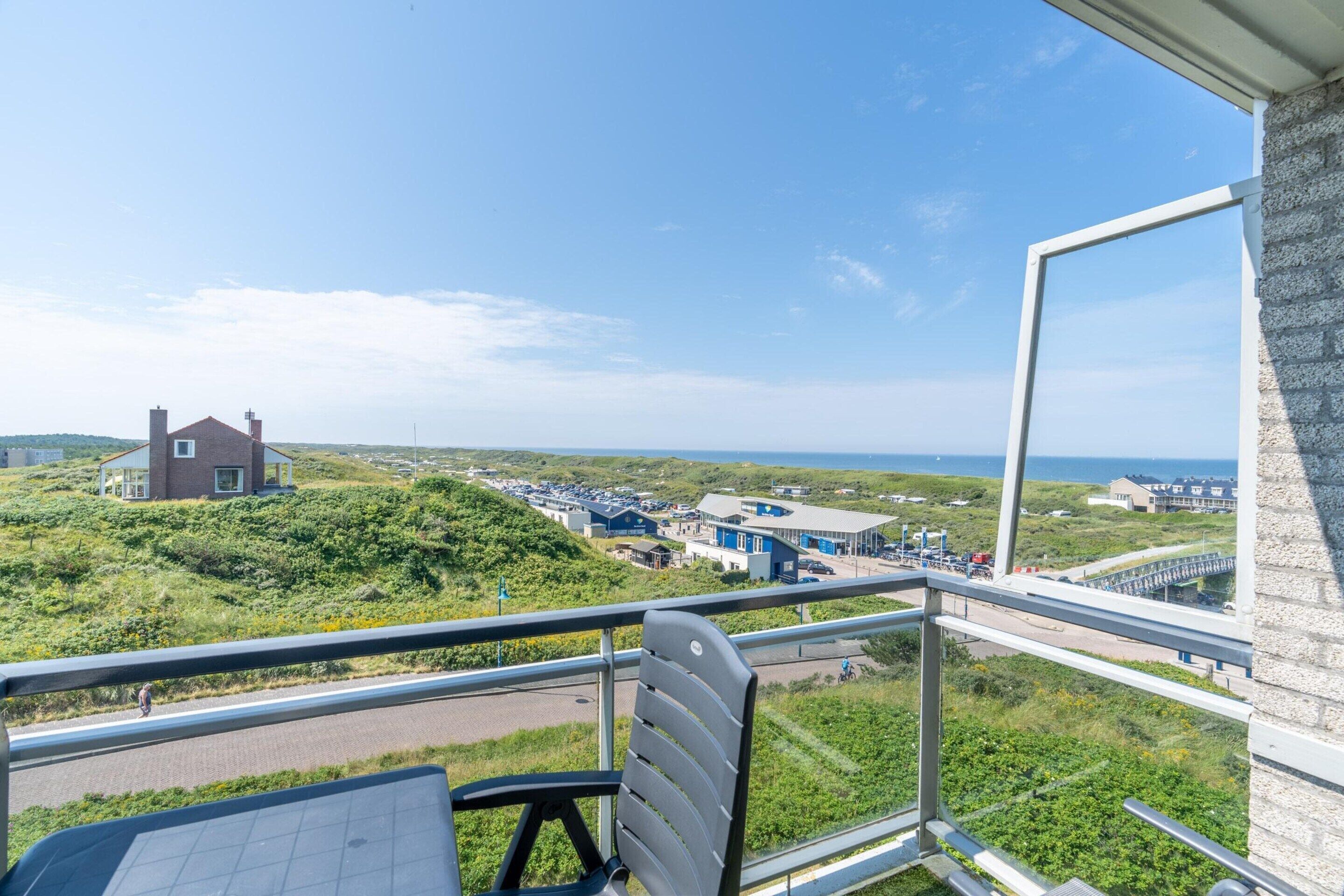 A balcony with a view of a coastal area, including a parking lot and buildings.