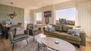 Un salon moderne comprenant un canapé, des fauteuils, une table basse et de grandes fenêtres donnant sur la campagne.