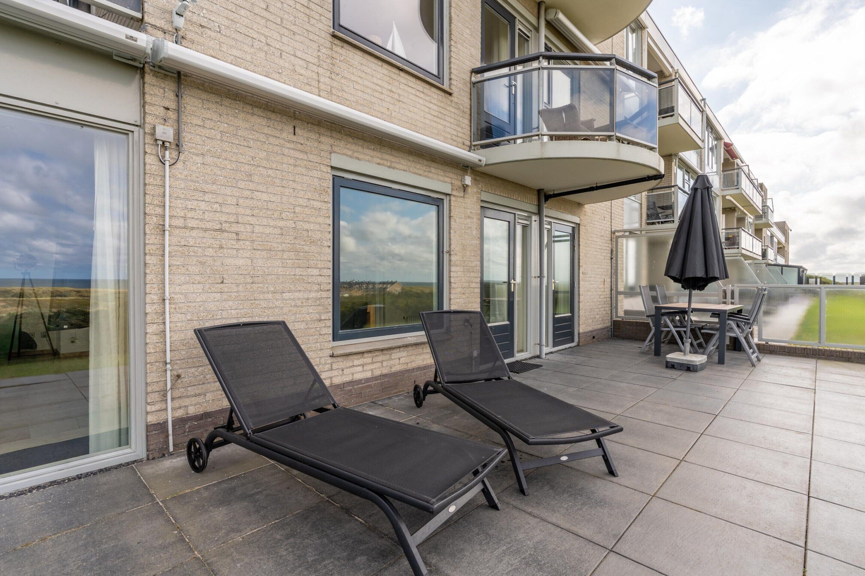 A balcony with two lounge chairs and a table, a glass door, and a view of the sea.