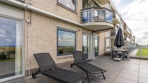Un balcone con due poltrone, un tavolo, una porta in vetro e vista sul mare.
