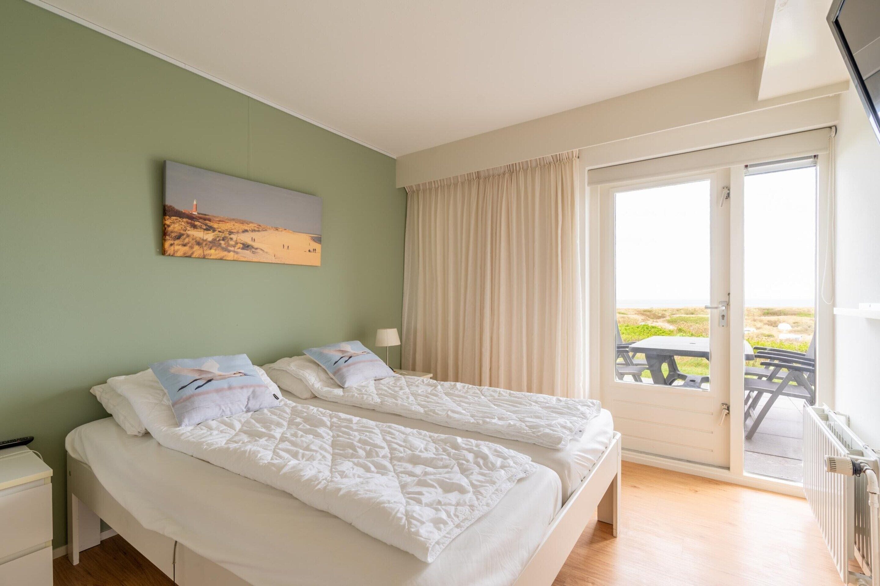 A room with two beds, a painting on the wall, a window with curtains, and a view of the outdoors.