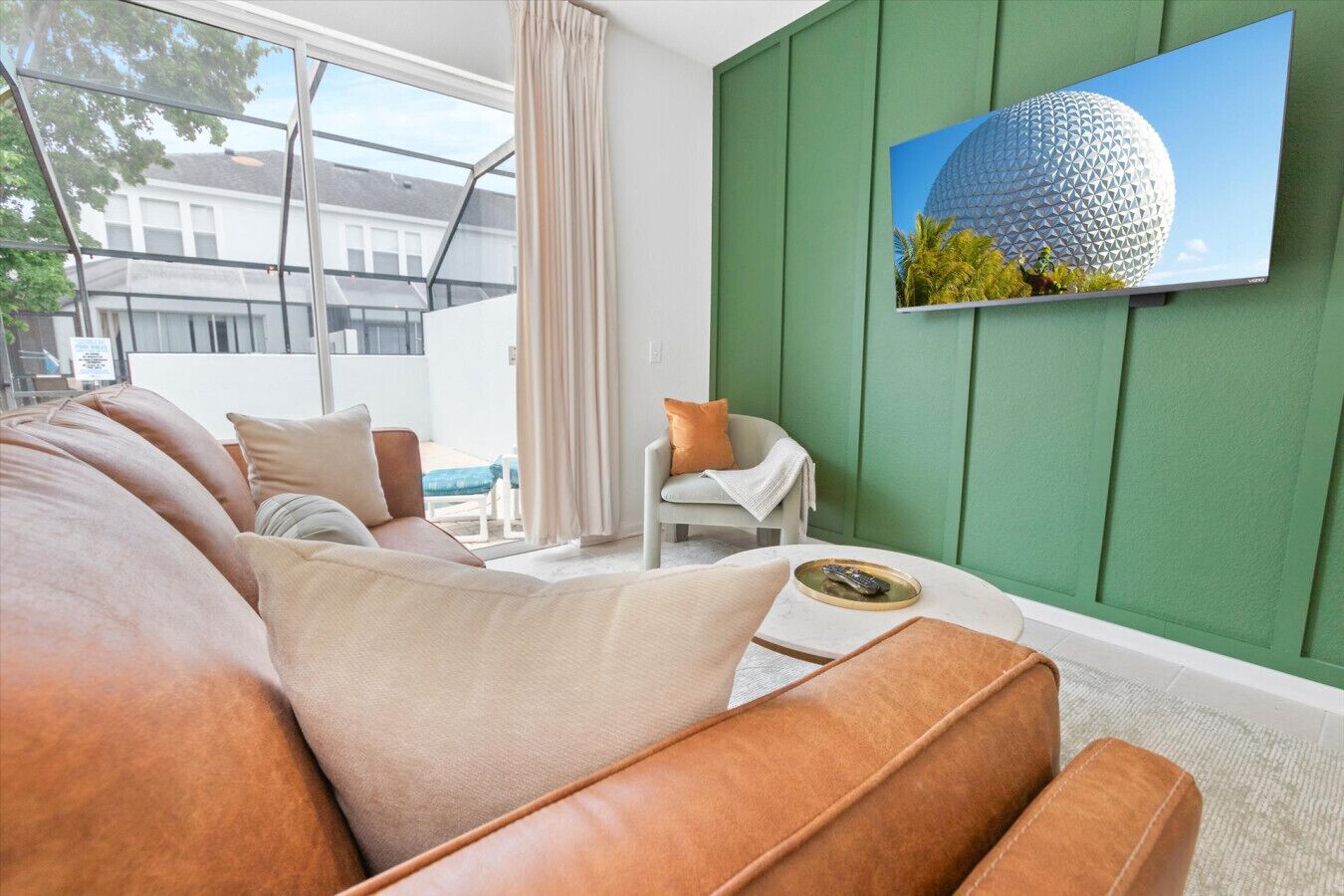 Ein modernes Wohnzimmer mit grüner Akzentwand, einem großen Fenster und einem Flachbildfernseher, der ein kugelförmiges Gebäude zeigt.