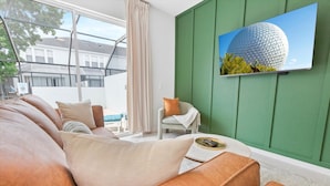 Een moderne woonkamer met een groene accentmuur, een groot raam en een flatscreen-tv waarop een bolvormig gebouw te zien is.
