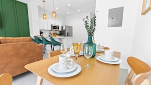 Een moderne eetruimte met een houten tafel gedekt voor twee personen, witte borden, een glas wijn en een decoratieve vaas.
