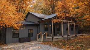 A rustic cabin with a porch, surrounded by autumn foliage.