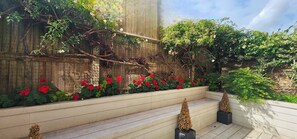 A garden with a wooden bench, a brick wall, and a variety of plants. - Stylish 2BR Apartment near Barons Court Station, West Kensington - Pass the Keys (London)