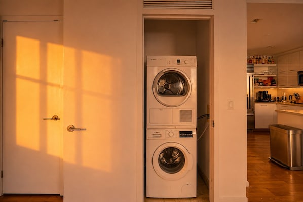 A laundry room with stacked washing machines and a kitchen area visible through an open door.