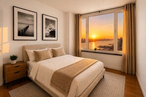 A bedroom with a large bed, a nightstand, a potted plant, and a window with a cityscape view.