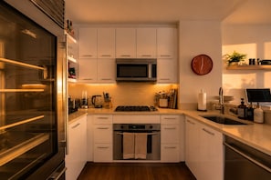 A modern kitchen with white cabinets, stainless steel appliances, and a wooden floor.