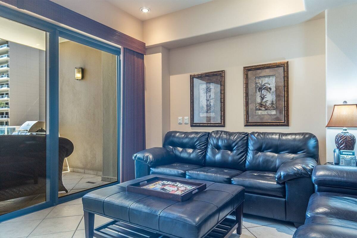 A modern living room with a leather sofa, a coffee table, and a TV. There are two framed artworks on the wall and a lamp on a side table.