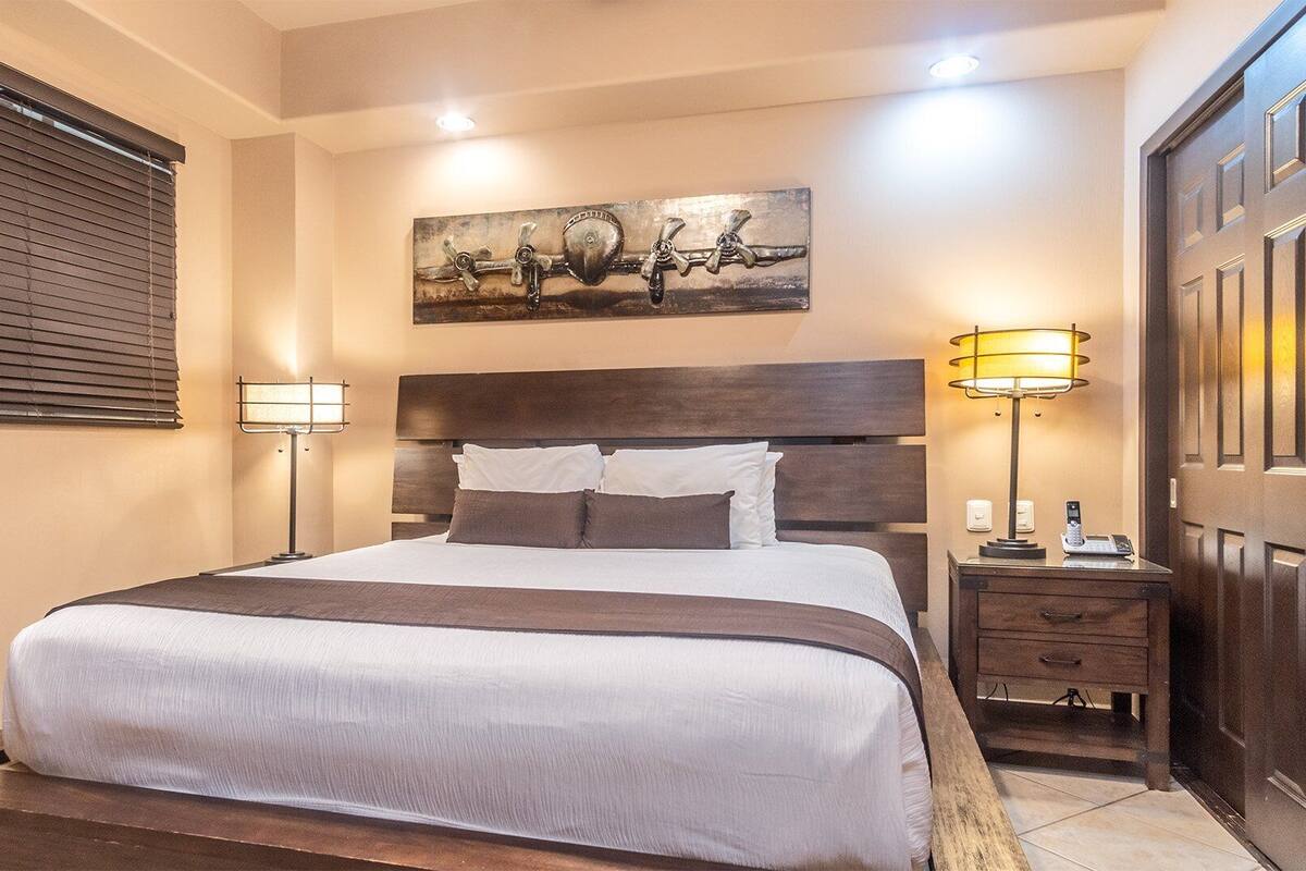 A hotel room with a large bed, two bedside tables, a painting on the wall, and a wooden door.