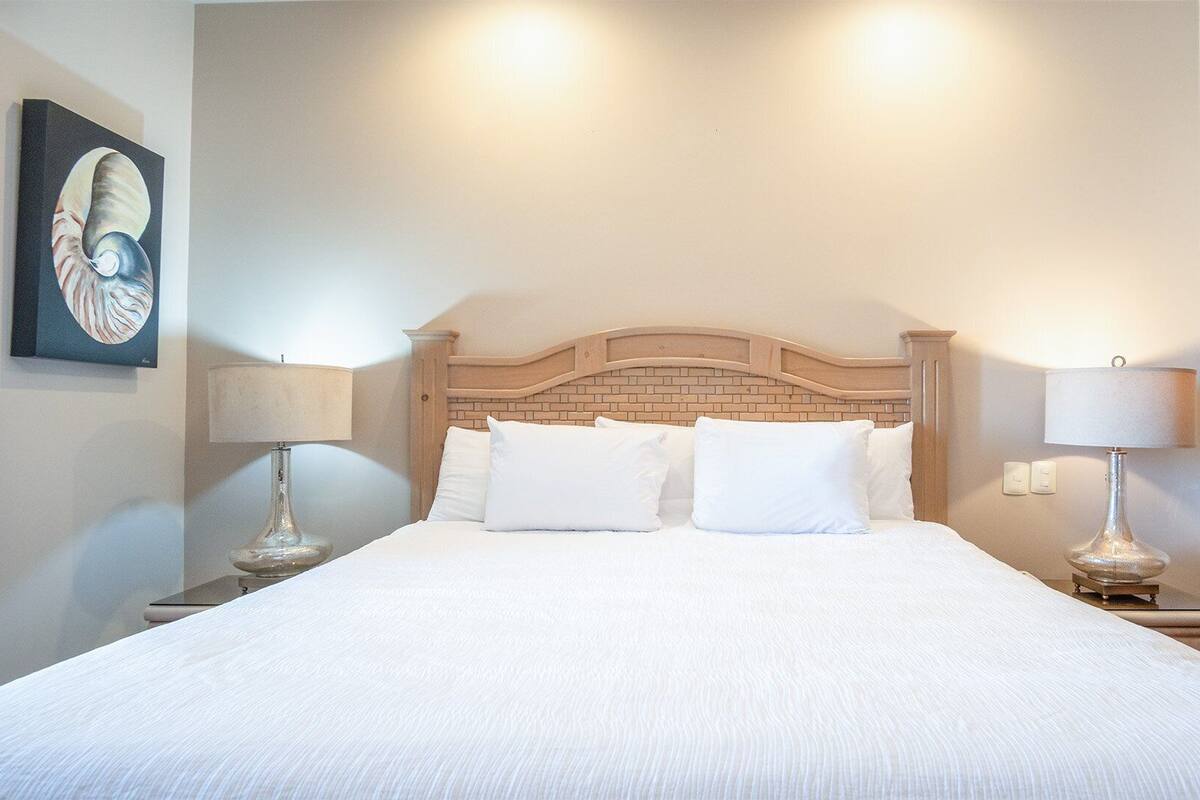 A neatly made bed with white linens, a brick-patterned headboard, and two bedside lamps on either side.