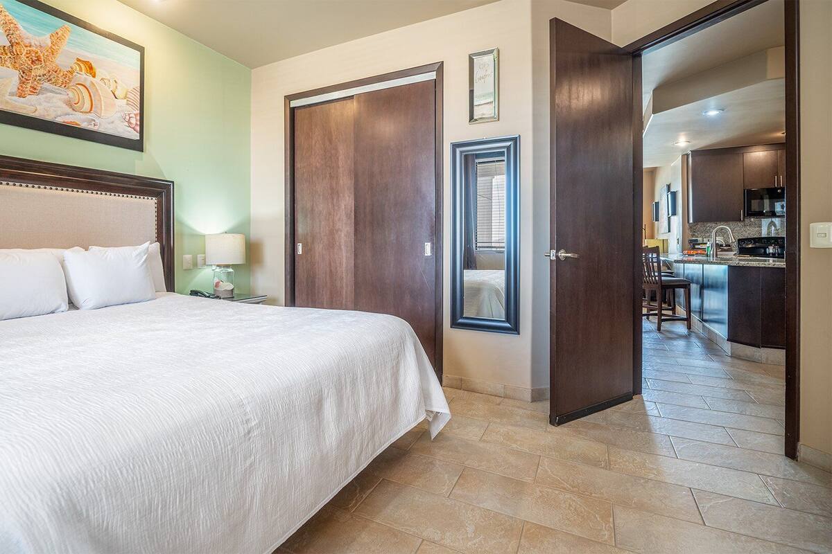 A hotel room with a large bed, a desk, and a view of the kitchen.