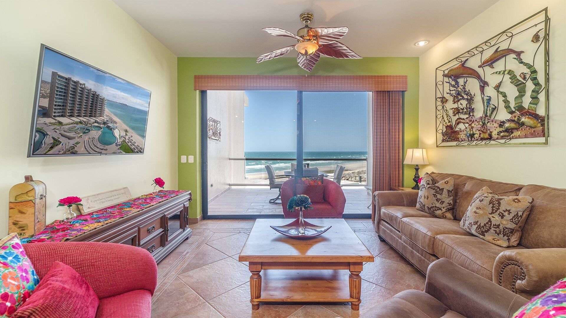 A living room with a view of the ocean, a ceiling fan, a table, and a couch.