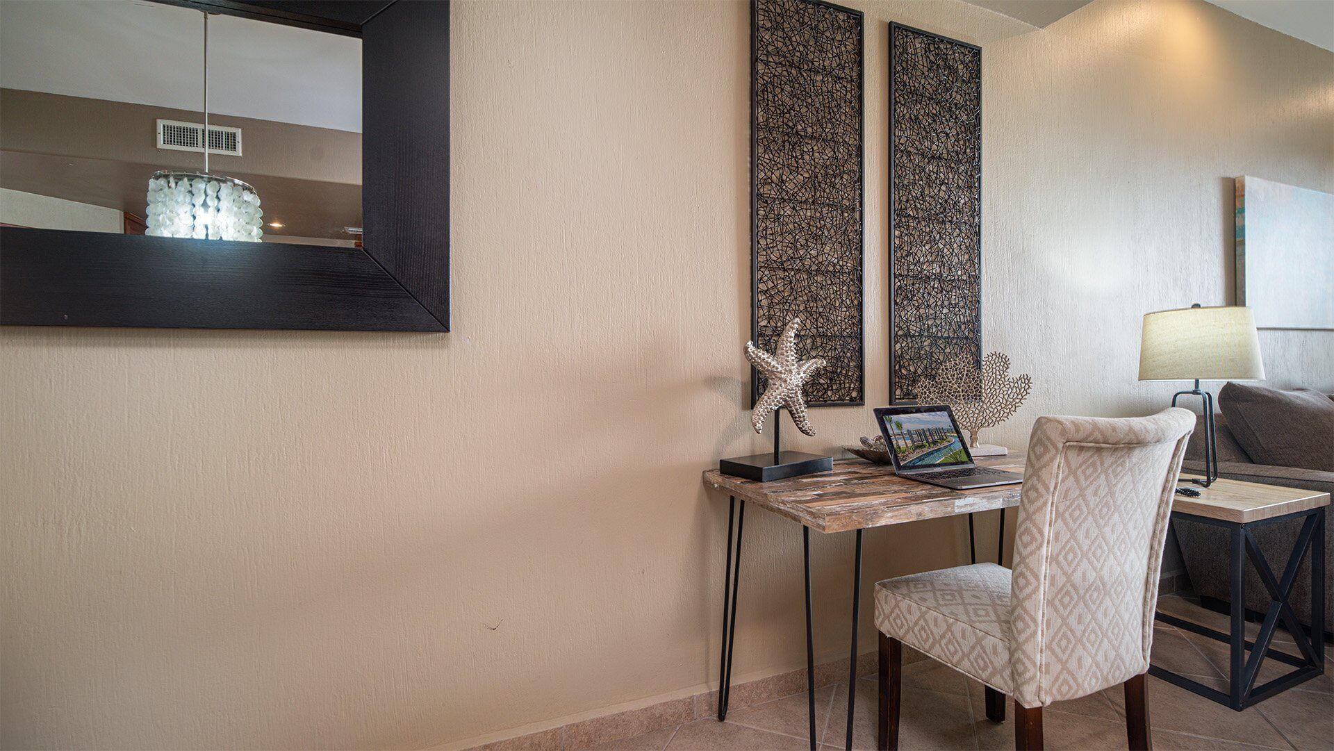A hotel room with a desk, chair, lamp, and artwork on the wall.