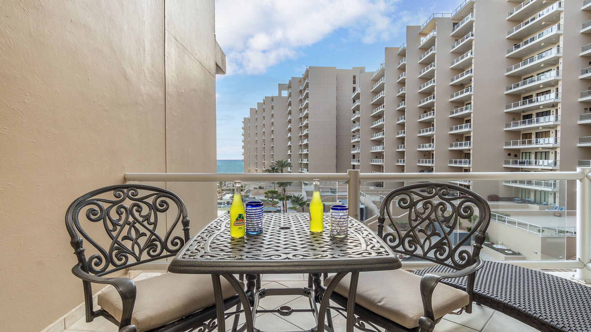 Un balcon avec une table et des chaises, donnant sur un immeuble de grande hauteur et une piscine.