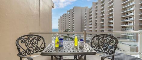 Un balcon avec une table et des chaises, donnant sur un immeuble de grande hauteur et une piscine.