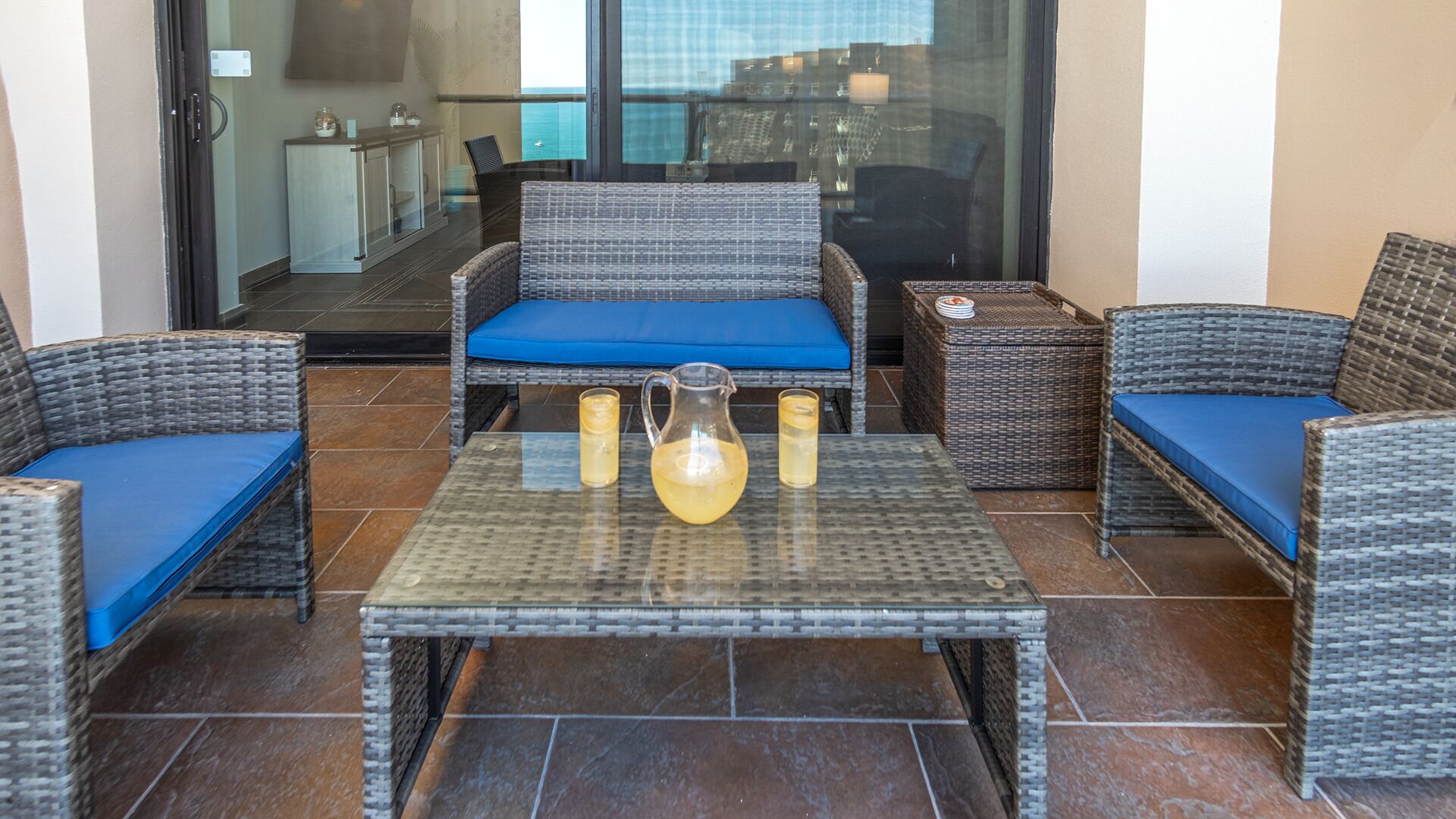 A patio area with wicker furniture, a glass table, and a pitcher of drink.