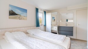 Ein Schlafzimmer mit zwei Betten, einem Fenster mit Vorhängen, einem Schminktisch und einem Spiegel.