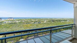 Ein Balkon mit freiem Blick auf eine Küstenlandschaft, darunter ein Strand und Gebäude in der Ferne.