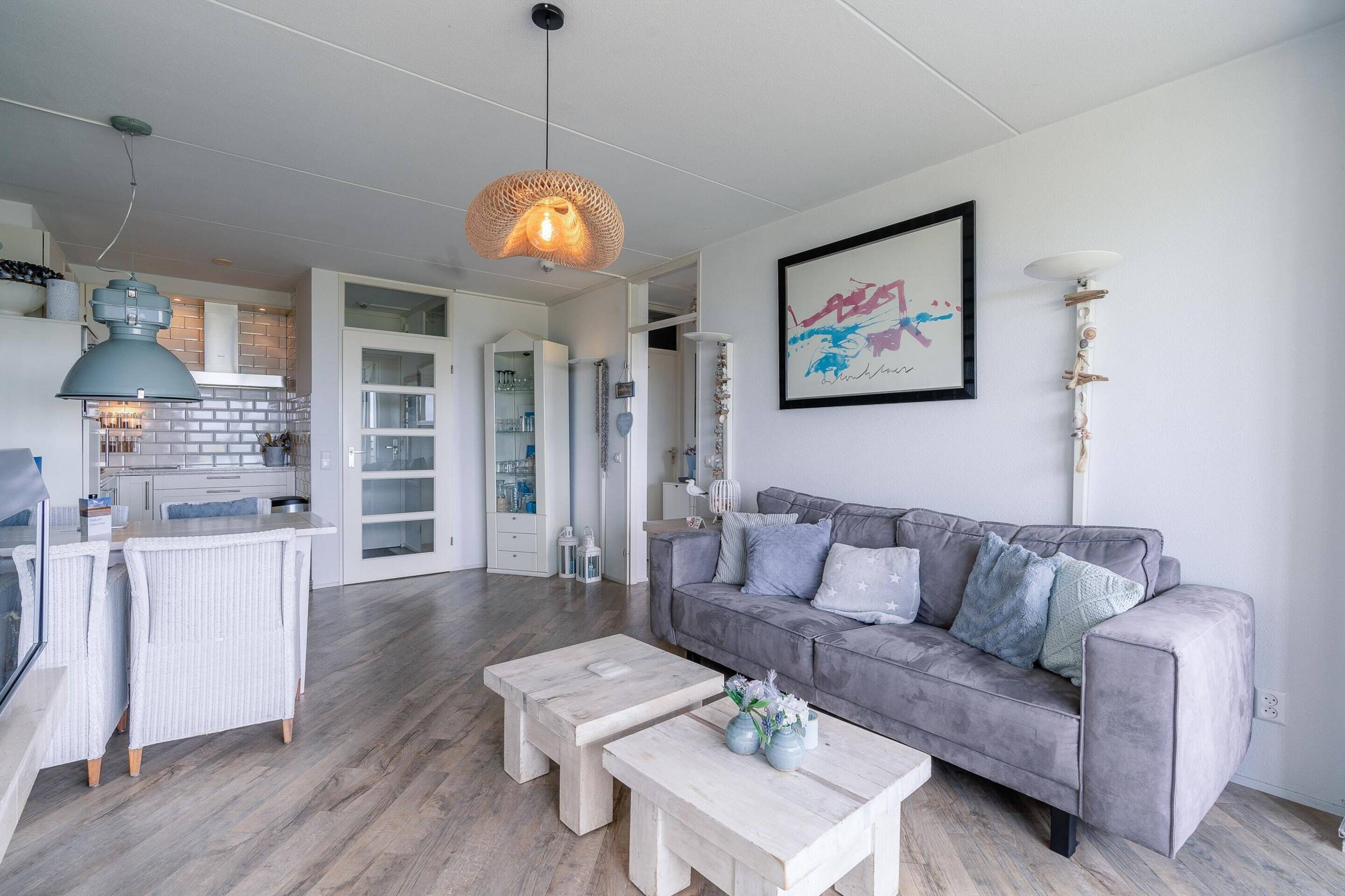 Ein modernes Wohnzimmer mit einem grauen Sofa, zwei weißen Couchtischen und einer Pendelleuchte.