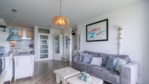 Ein modernes Wohnzimmer mit einem grauen Sofa, zwei weißen Couchtischen und einer Pendelleuchte.
